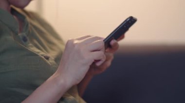 Oturma odasındaki kanepede otururken akıllı telefon kullanarak sosyal medyayı kontrol eden Asyalı kadını kapat..