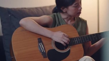 Evde otururken gitar öğrenmeye çalışan Asyalı kadın..