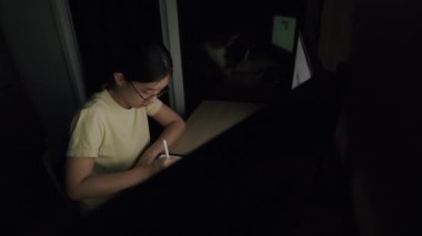 Asyalı iş kadını, gece bir ev ofisinde bir tablet üzerinde çalışmalar çizdi, haber yayınlarını kaydırdı ve çalışma planı için internet bilgilerini araştırdı..