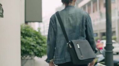 Maske takan yakışıklı Asyalı adam salgın sırasında sokakta yürürken omuz çantası taşıyor..