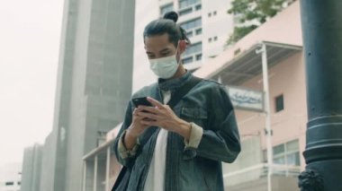 Genç Asyalı hippi şehirde sokakta dikilirken akıllı telefon kullanıyor..