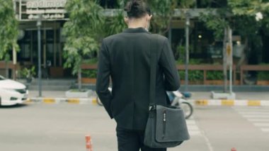 Asyalı iş adamı sokakta yürürken omuz çantası taşıyor..
