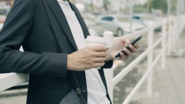 Genç bir işadamı, şehirde çitin yanında dururken akıllı telefon kullanıyor..