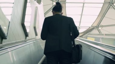 Asyalı iş adamı sabah metroda yürüyen merdivende duruyor. Ofise gidiyor..