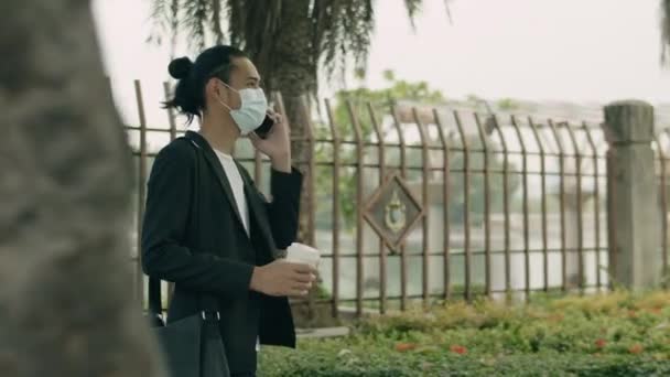 Azjatycki Biznesmen Masce Chirurgicznej Trzymający Filiżankę Kawy Rozmawiający Przez Telefon — Wideo stockowe