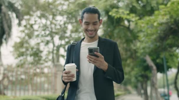 Uśmiechnięty Biznesmen Azjatycki Patrząc Smartfona Podczas Spaceru Ulicy Biura Rano — Wideo stockowe