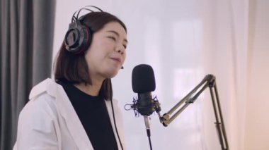 Genç Asyalı kadın podcaster bir podcast kaydederken mikrofona konuşuyor ve evde sosyal medya için canlı yayın içeriği.