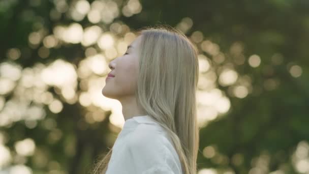 日落时分 一位年轻貌美的亚洲女子闭上了眼睛 享受着公园里的微风草甸 — 图库视频影像