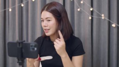 Genç Asyalı kadın güzellik blogcusu makyaj sanatçısı akıllı telefon eğitim videosuna kayıt yapıyor. Kozmetik, sosyal medyada bir aboneye uygulanır..