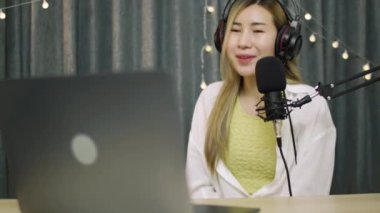 Asyalı kadın etkileyicisi sosyal medya için podcast mikrofon kullanarak bir vlog kaydediyor ve canlı yayın içeriğini kaydediyor.