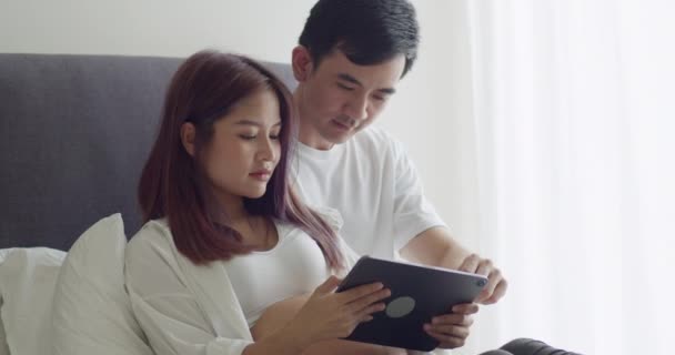 年轻的亚洲丈夫带着怀孕的妻子在家里感到快乐 用平板电脑 — 图库视频影像