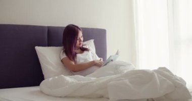 Mutlu Asyalı hamile eş, doğmamış bir çocuğa kitap okurken yatak odasında yatıyordu..