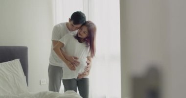 Mutlu Asyalı koca, güzel yatak odalarının penceresinde dikilirken karısının karnına dokunuyor..