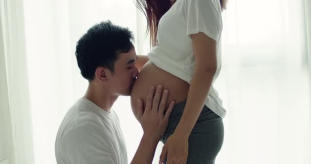 Boldog Ázsiai Férj Megcsókolja Felesége Terhes Hasát Miközben Egy Ablak — Stock videók