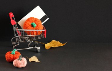 Karanlık arka planda sonbahar satış düzeni, Kara Cuma, bozuk paraların yanında alışveriş sepeti, turuncu iplik kabakları ve yapraklar..