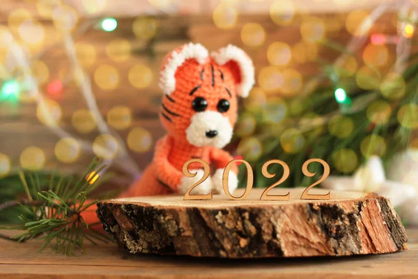 crocheted tiger sitting with a gift on a wooden background with branches of a christmas tree in the background