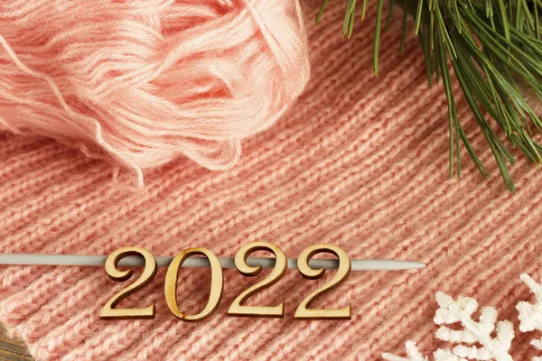 Mutlu yıllar, 2022 örgü bir süveterin şeftali arkaplanı ve bir noel ağacının dalı üzerine, narin bir kart..