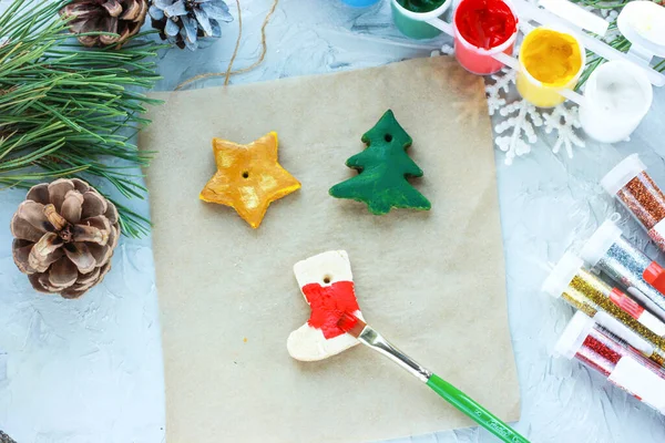 Un pincel con pintura roja pinta un calcetín de Navidad, juguetes de bricolaje para el Año Nuevo, decoración creativa para un árbol de Navidad hecho de masa de sal — Foto de Stock