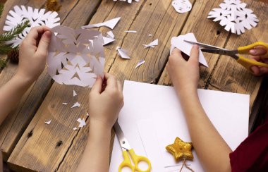 Çocukların elleri evdeki kağıttan kar tanelerini ahşap bir arka planda kesiyor..