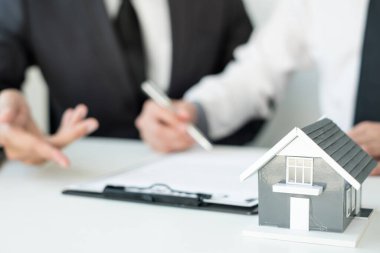 Ev modeli olan bir emlakçı ev sigortası almak için müşterilerle konuşuyor. Gayrimenkul Ev Sigortası.