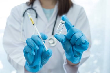 COVID-19. Kadın doktor laboratuarda iğne ve aşı şişesini yakından tutuyor..
