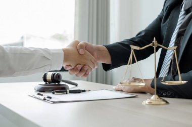 Hukuk bürosunda çalışan profesyonel avukatların tokalaşması için teraziler, adalet terazileri, yargıç tokmağı ve dava belgeleri var. Hukuk ve adalet kavramları.