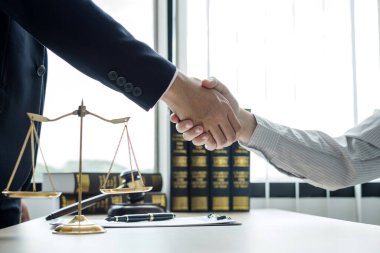 Hukuk bürosunda çalışan profesyonel avukatların tokalaşması için teraziler, adalet terazileri, yargıç tokmağı ve dava belgeleri var. Hukuk ve adalet kavramları.