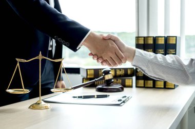 Hukuk bürosunda çalışan profesyonel avukatların tokalaşması için teraziler, adalet terazileri, yargıç tokmağı ve dava belgeleri var. Hukuk ve adalet kavramları.