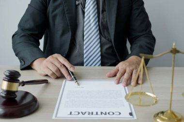 Profesyonel erkek avukatlar bir hukuk bürosunda çalışır. Teraziler, adalet terazileri, yargıç tokmağı ve dava belgeleri vardır. Hukuk ve adalet kavramları.