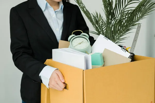 A woman office worker is unhappy with being fired from a company packing things into cardboard boxes. The Young woman was stressed and disappointed by being fired. concept of layoffs and unemployment.