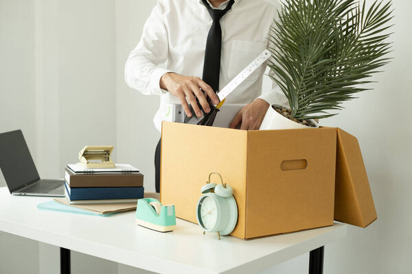 A male office worker is unhappy with being fired from a company packing things into cardboard boxes. The young man was stressed and disappointed by being fired. concept of layoffs and unemployment.