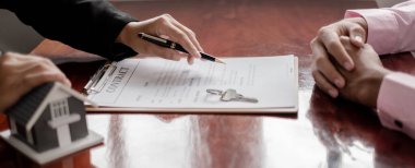 Ev modeli olan bir emlakçı ev kiralamak ve ev sigortası almak için müşterilerle konuşuyor. Ev kiralama ve sigorta konsepti.