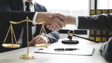 Hukuk bürosunda çalışan profesyonel avukatların tokalaşması için teraziler, adalet terazileri, yargıç tokmağı ve dava belgeleri var. Hukuk ve adalet kavramları.