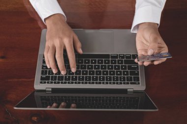 İş adamının elinde bir kredi kartı var ve online alışveriş ve internet ödemeleri için bir laptop kullanıyor..