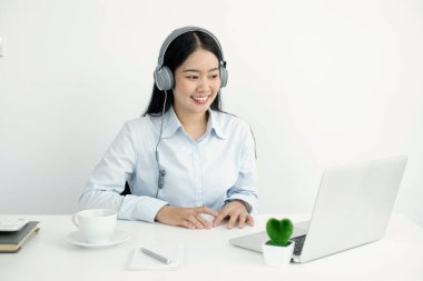 Video çağrısı, kulaklık takan genç bir Asyalı kadın, internetteki uzun mesafeli video ile iletişim kuruyor, dijital laptop ekranına bakıyor, bir arkadaşıyla mutlu bir şekilde selamlaşıyor..