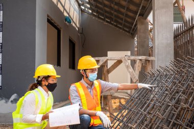 Erkek ve kadın mühendis veya mimarlardan oluşan bir ekip açık hava inşaat çalışmalarını inceliyor ve inceliyor.