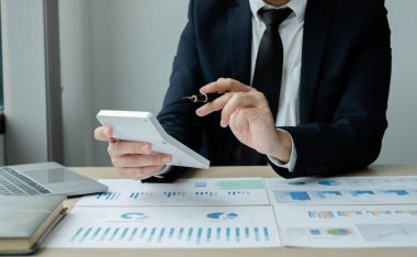 İş adamının eli masalarında oturup yatırımlarıyla ilgili sonuçları gösteren finansal grafikleri hesaplıyor, başarılı bir iş büyüme süreci planlıyor.