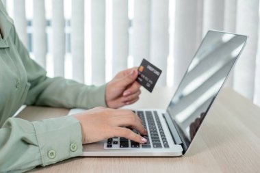 İş kadınının elinde bir kredi kartı var ve ofisteki online alışveriş ve internet ödemeleri için bir dizüstü bilgisayar kullanıyor..