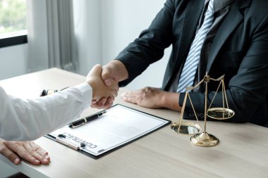 Hukuk bürosunda çalışan profesyonel avukatların tokalaşması için teraziler, adalet terazileri, yargıç tokmağı ve dava belgeleri var. Hukuk ve adalet kavramları.