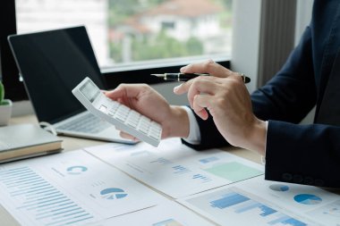 İş adamının eli masalarında oturup yatırımlarıyla ilgili sonuçları gösteren finansal grafikleri hesaplıyor, başarılı bir iş büyüme süreci planlıyor.