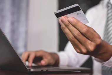 İş adamının elinde bir kredi kartı var ve online alışveriş ve internet ödemeleri için bir laptop kullanıyor..
