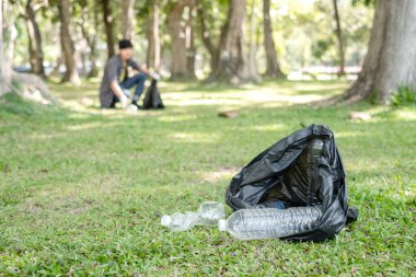 Plastik şişe. Genç Asyalı erkekler plastik şişeleri toplar, parkları temizlemek, kirlilikten kaçınmak, çevreye ve ekosisteme dost olmak için çöpleri siyah çöp torbalarına koyarlar..