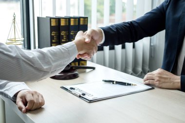 Hukuk bürosunda çalışan profesyonel avukatların tokalaşması için teraziler, adalet terazileri, yargıç tokmağı ve dava belgeleri var. Hukuk ve adalet kavramları.