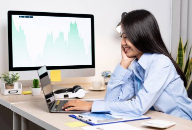 Ofiste çalışırken mutlu ve neşeli bir gülümsemeyle dizüstü bilgisayarda çalışan Asyalı kadın..