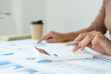 Finans sektöründe çalışan bir kadın evinde oturup yatırımlarının sonuçlarını gösteren mali grafikleri hesaplar ve iş büyümesinin adımlarını planlar..