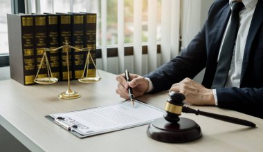 Profesyonel erkek avukatlar bir hukuk bürosunda çalışır. Teraziler, adalet terazileri, yargıç tokmağı ve dava belgeleri vardır. Hukuk ve adalet kavramları.