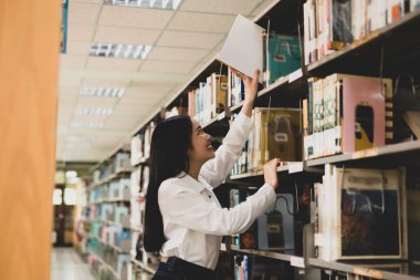 Genç Asyalı kadınlar akademik ve eğitimsel benliklerini araştırmak ve geliştirmek için üniversite kütüphanelerinin masaları ve koridorları hakkında kitaplar arıyor ve okuyorlar..