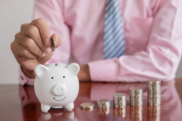 The hand of a businessman puts coins in a piggy bank, saves money with coins, steps into a successful growth business, and saves for retirement concept.