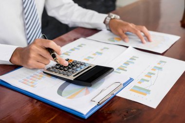 İş adamı masalarında oturur ve başarılı iş büyümesi sürecini planlayan yatırımlarının sonuçlarını gösteren mali grafikleri hesaplar.