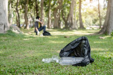Plastik şişe. Genç Asyalı erkekler plastik şişeleri toplar, parkları temizlemek, kirlilikten kaçınmak, çevreye ve ekosisteme dost olmak için çöpleri siyah çöp torbalarına koyarlar..